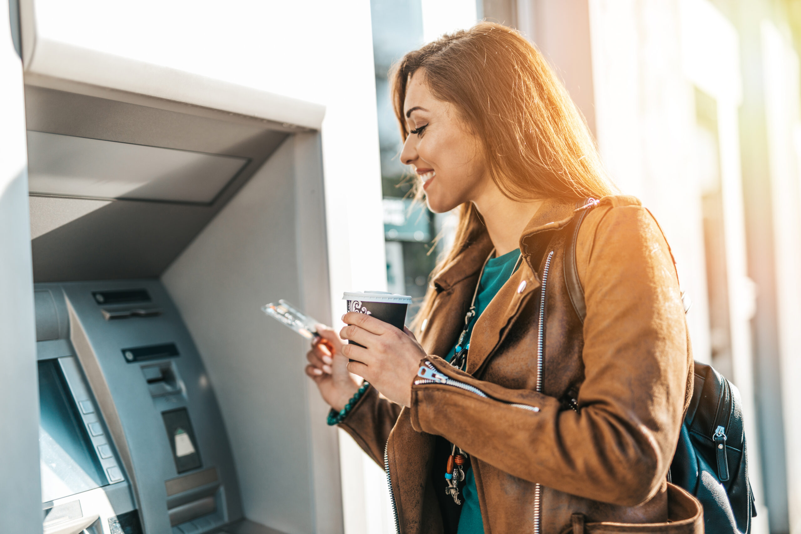 happy-young-adult-woman-standing-front-atm-machine-smiling-holding-credit-debit-card women at an ATM in bank