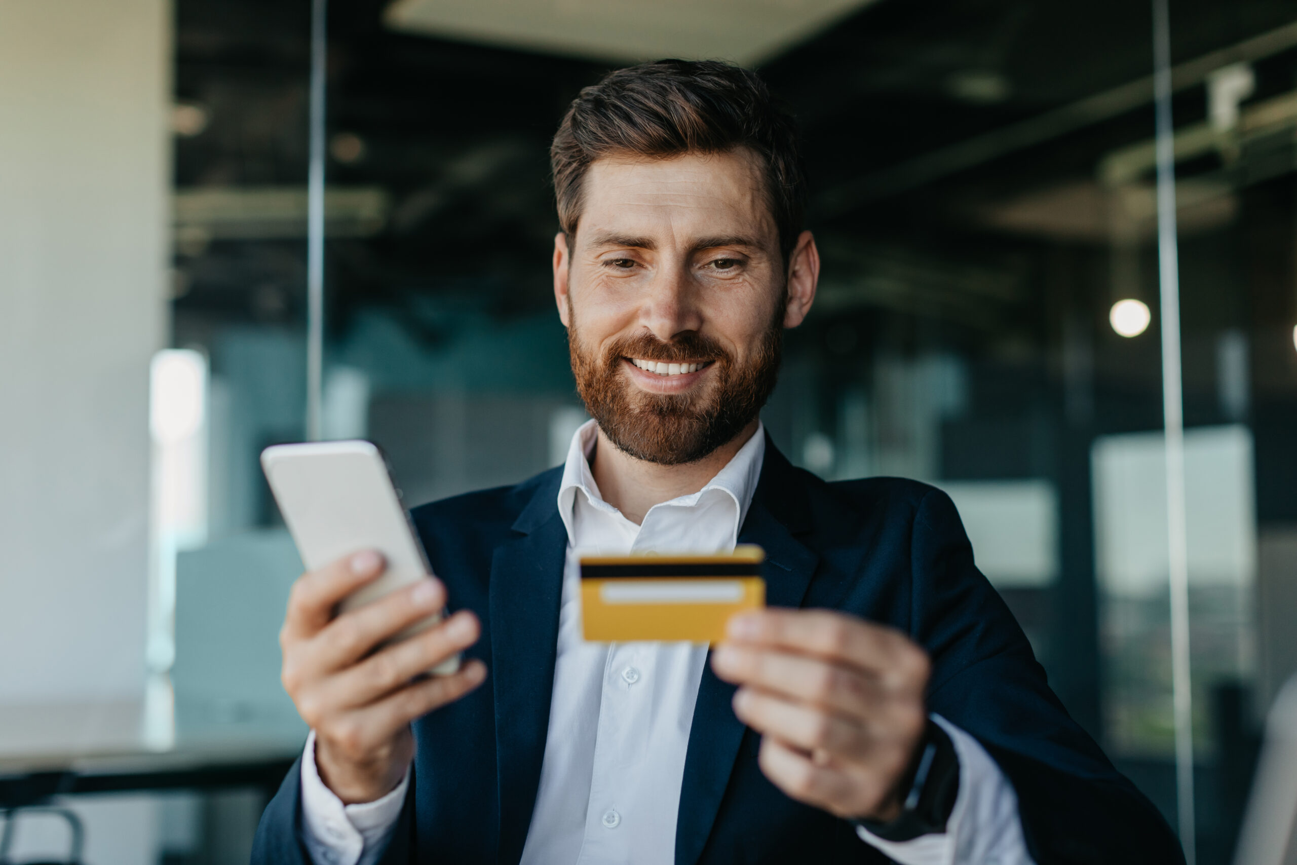 Online banking concept. Happy caucasian general manager making online payment on smartphone, sitting in office Yellow-vest worker with headphones in an airport